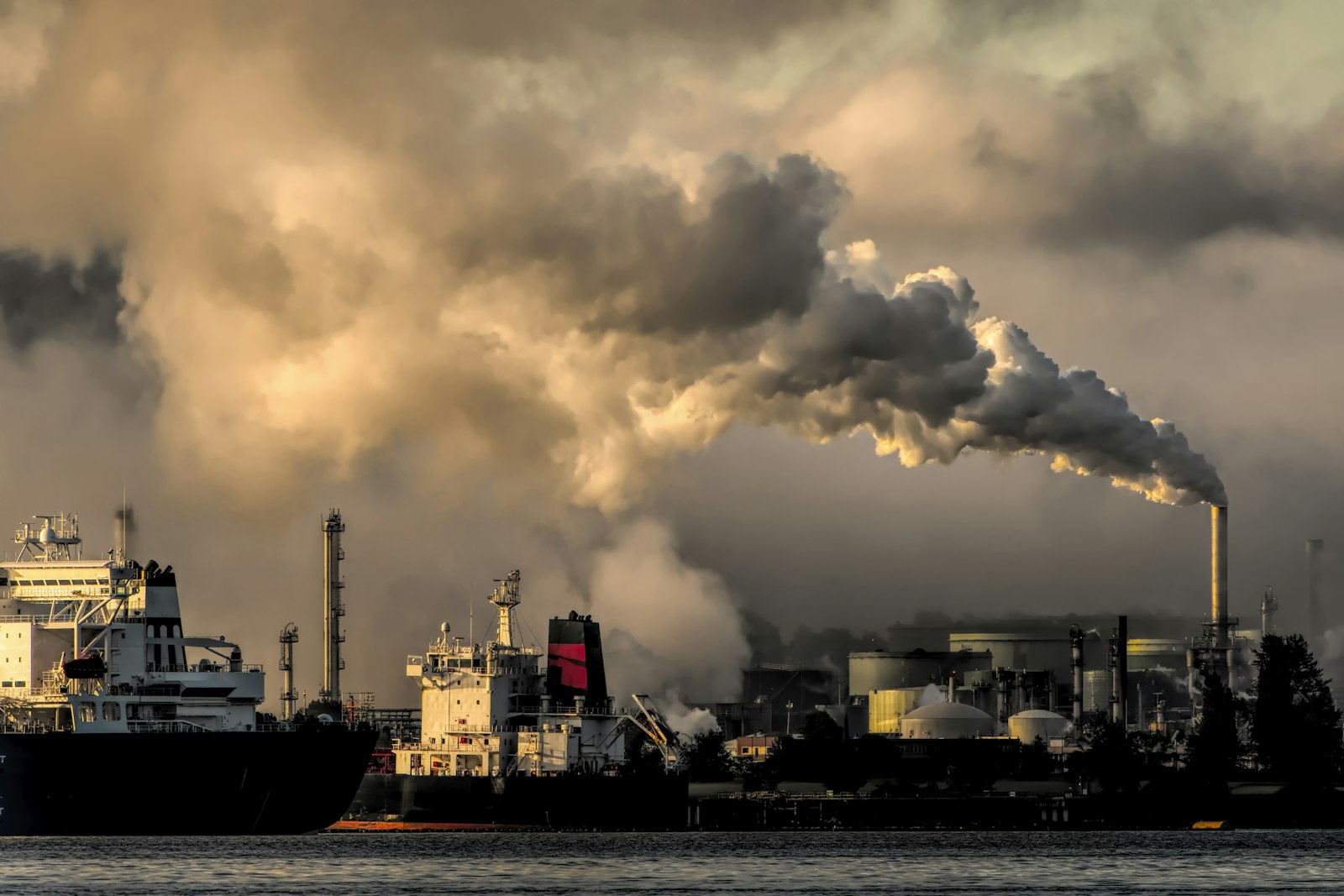 Smokestacks at an industrial harbour releasing plumes at dusk