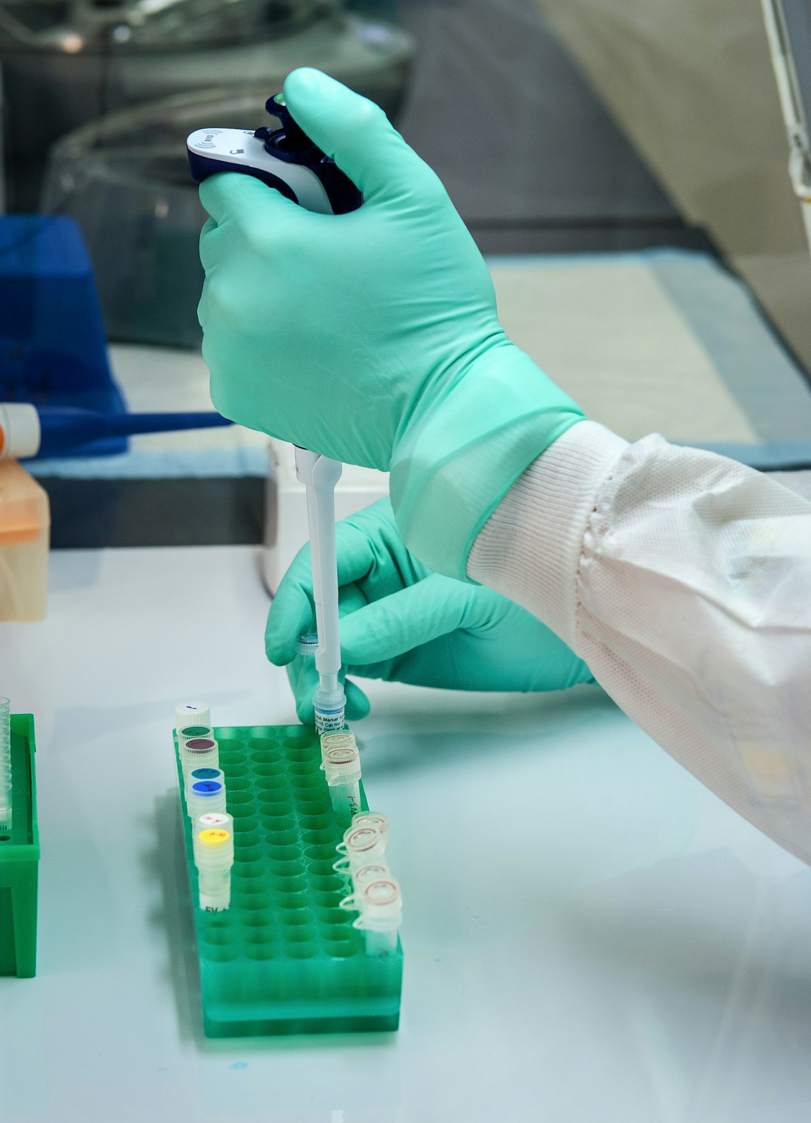 A gloved researcher pipetting samples into a rack of vials in a laboratory