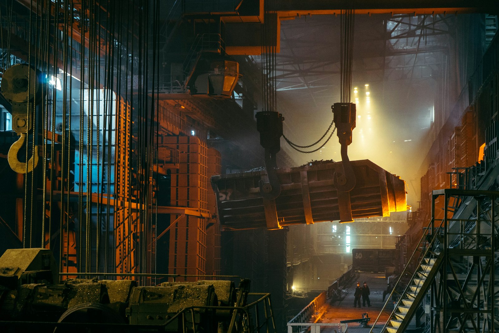 A crane lifting a glowing ladle of molten steel inside a steelworks